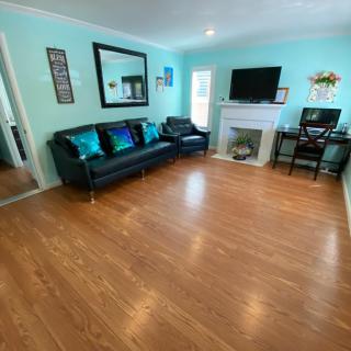 A spacious and brightly lit living room featuring a black sofa, television, and fireplace on a hardwood floor.