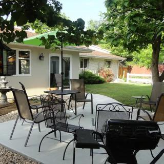 A cozy backyard patio with seating and a grill, surrounded by lush greenery.