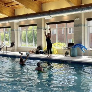 An indoor aquatic fitness class with participants exercising in a swimming pool.