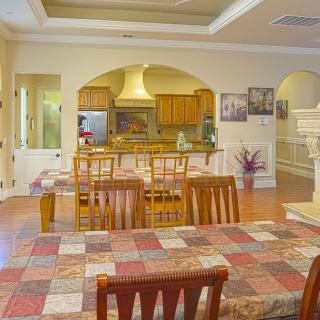 A cozy dining area with wooden furniture leading to a kitchen, featuring a colorful tablecloth and open design.