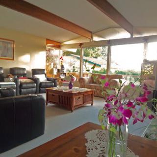 A cozy living room with ample sunlight, featuring comfortable sofas, a wooden coffee table, and a vase of flowers.