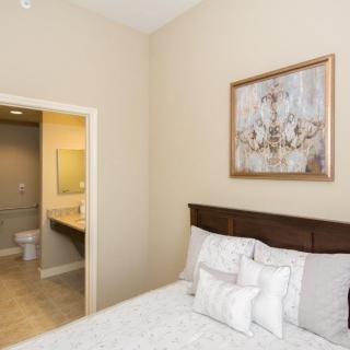 A cozy bedroom with an adjacent bathroom, featuring a bed with white bedding and a decorative painting on the wall.