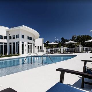 A luxurious modern building with a swimming pool and outdoor seating under a sunny sky.