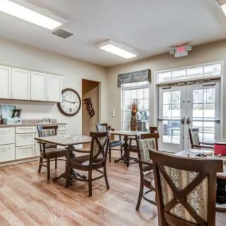 A cozy dining area with a kitchenette, featuring wooden flooring and seating arrangements.