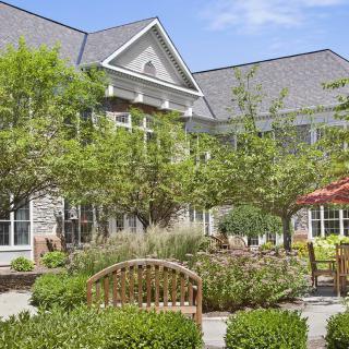 A serene garden with a bench and lush greenery in front of a large residential building.