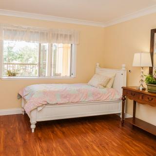 A cozy bedroom with a single bed, wooden floor, and a window letting in natural light.