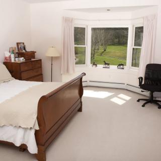 A cozy bedroom with a large window providing natural light, featuring wooden furniture and a comfortable atmosphere.
