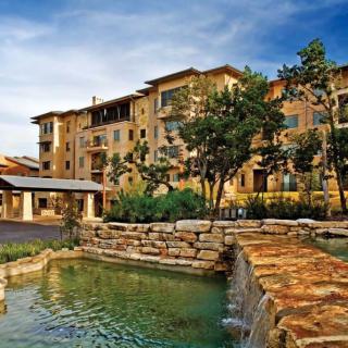 A scenic view of a multi-story apartment building with a stone pathway and water feature in the foreground.