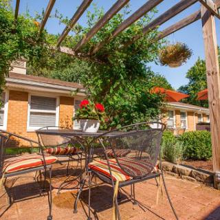 A cozy outdoor patio with a table and chairs, surrounded by greenery and vibrant flowers.