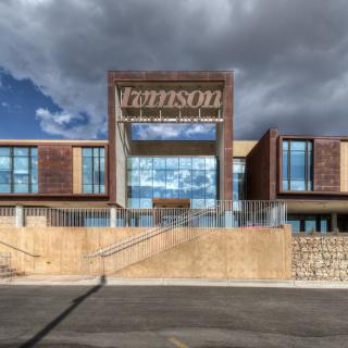 A modern building with large windows and a prominent entrance under a cloudy sky.