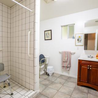 An accessible bathroom with a tiled shower area, equipped with a shower chair and a wooden vanity with a mirror.