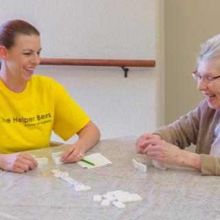 A caregiver and an elderly person enjoying a game together at the table.