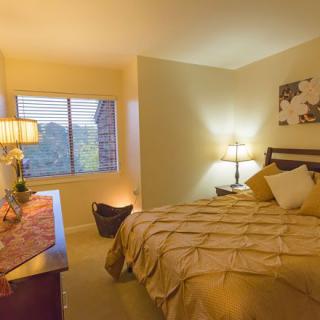 A cozy bedroom with warm lighting, featuring a neatly made bed and a large window.