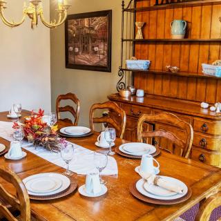 A cozy dining room with a wooden table set for dinner, featuring elegant dinnerware and surrounded by matching chairs.