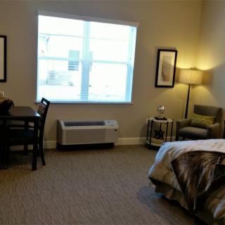 A cozy bedroom with a bed, chair, lamp, and window.