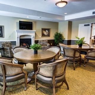 A cozy and elegantly furnished dining area with round tables, comfortable chairs, and decorative plants.