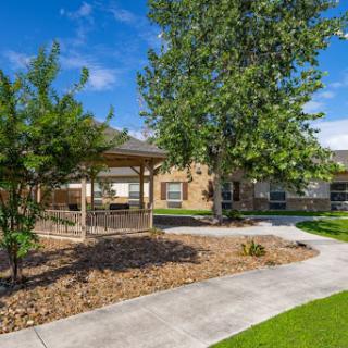 A serene outdoor area featuring a pathway, trees, and a gazebo adjacent to a building.