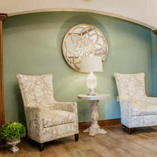 A cozy and inviting corner of a living room featuring stylish chairs, a lamp, and decorative wall art.