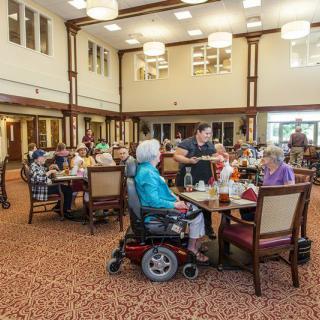 A group of elderly individuals enjoying a meal and socializing in a spacious dining area.