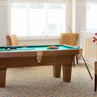 A cozy game room featuring a billiards table with cue sticks and chairs around it.