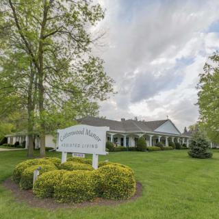 A house with a front yard and a sign surrounded by trees under a cloudy sky.