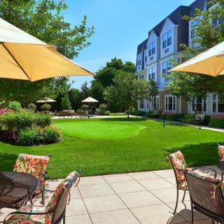 A sunny garden patio with furniture and umbrellas overlooking a well-manicured lawn.