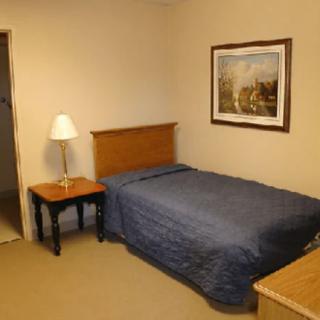 A modestly furnished bedroom with a single bed, nightstand, and lamp.