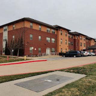 A modern residential building with brick exterior and a parking area under a cloudy sky.