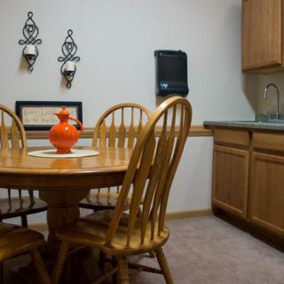A cozy kitchen nook with a wooden dining table and chairs, featuring a bright orange vase as a centerpiece.