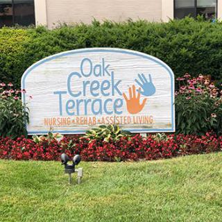 Sign reading 'Oak Creek Terrace' surrounded by greenery and flowers.