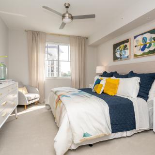 A bright, modern bedroom featuring a stylish bed with navy and white bedding, decorative pillows, and abstract artwork on the walls.