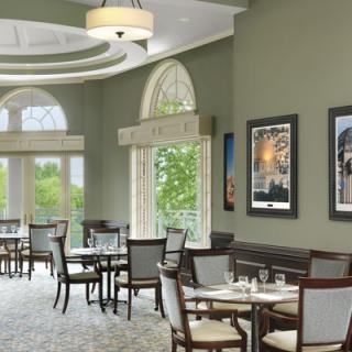 A spacious and elegantly decorated restaurant dining area with tables and chairs, featuring large windows and framed artwork on the walls.
