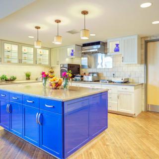 A modern kitchen featuring a vibrant blue island, wooden floors, and stylish pendant lighting.