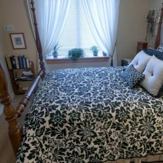 A cozy bedroom with a patterned bedspread and pillows, featuring a window with sheer curtains.