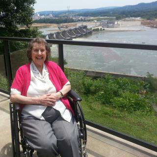 A woman in a wheelchair smiling with a scenic view in the background.