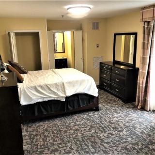 A well-furnished bedroom featuring a bed, dresser with mirror, and carpeted floor.
