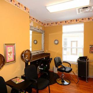 A cozy hair salon interior featuring chairs, mirrors, and a hair dryer, with warm decor and natural light from the window.