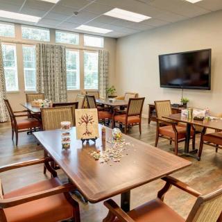 A well-lit dining room with multiple tables and chairs, featuring a large television on the wall.