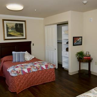 A cozy bedroom with a single bed, artwork on the wall, and an open closet.