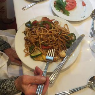 A plate of noodles with vegetables served at a restaurant table.