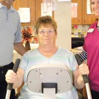 A woman using exercise equipment with the assistance of two therapists.