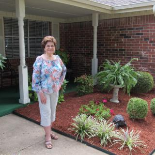 A woman stands in front of a landscaped garden next to a house with a brick wall.