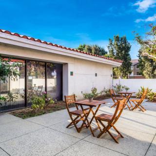 A sunny patio area with wooden tables and chairs, surrounded by a garden setting.