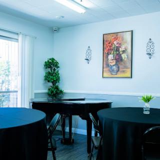 An elegantly decorated dining area with black tablecloths, a piano, and wall art.