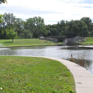 A peaceful park scene with a pond and curved pathway surrounded by trees and grass.