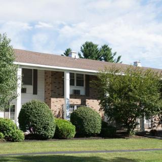 A suburban apartment building with a brick facade, surrounded by trees and shrubs.