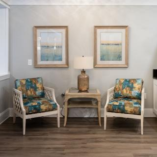 A cozy living room setup with two patterned armchairs, a lamp on a wooden side table, and framed artwork on the wall.