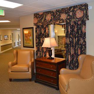 A cozy lounge area featuring two leather chairs, a wooden table with a lamp, and decorative curtains.