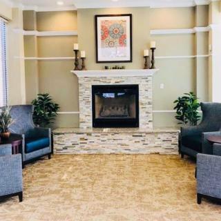 A cozy living room with a central fireplace, surrounded by elegant chairs and decorated with indoor plants and framed art.