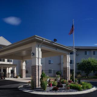 A building with a covered entrance and a flagpole, surrounded by landscaping under a clear blue sky.